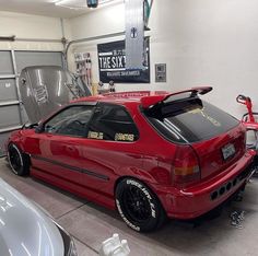 a red car parked in a garage next to two other cars and one has the hood up