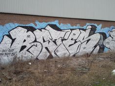 graffiti on the side of a brick wall in an area with dry grass and weeds