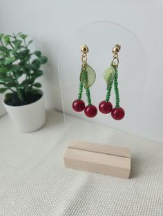 two cherries hanging from the back of a pair of earrings on a stand next to a potted plant