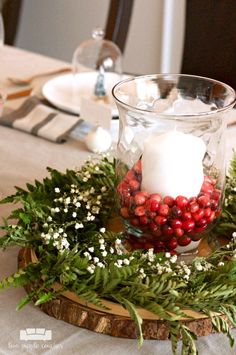 a candle is sitting in a glass bowl with greenery and berries on the table