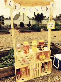 an outdoor lemonade stand with jars and bottles on it's shelf, in the middle of a gravel area