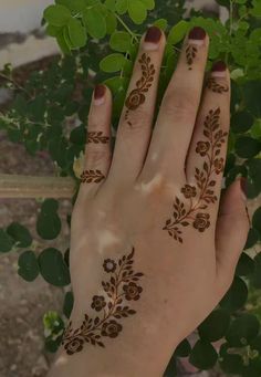 a woman's hand with henna tattoos on it and green leaves in the background