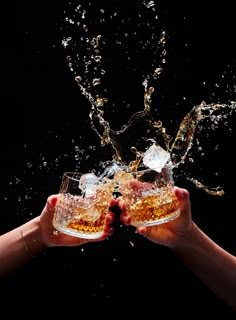 two hands holding glasses filled with beer splashing out of the top to the bottom