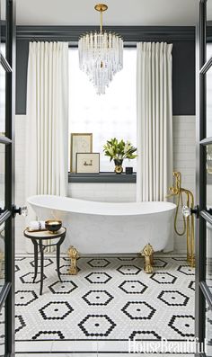 a white bath tub sitting under a chandelier next to a window with curtains