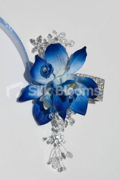 a blue flower and crystal broochle on a white surface with water droplets around it