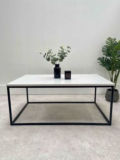 a white table with two black vases on it and a plant in the background