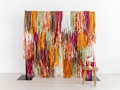 a chair sitting in front of a curtain with multicolored fringes on it