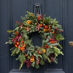 a christmas wreath hanging on the front door of a house with pine cones and berries