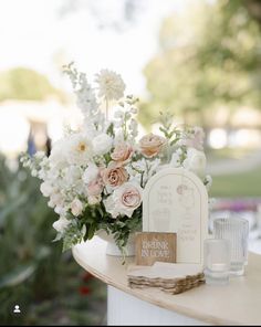 a vase filled with white and pink flowers on top of a table next to a sign