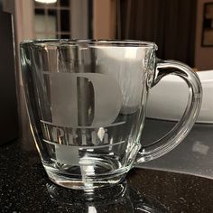 a clear glass mug with the letter d on it sitting on a counter top next to a window