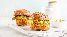 two burgers sitting on top of a white plate next to a bowl of guacamole