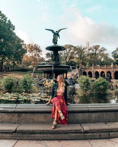 a man and woman standing in front of a fountain with a bird statue behind them