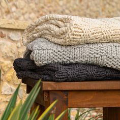 a stack of blankets sitting on top of a wooden table next to a plant and stone wall