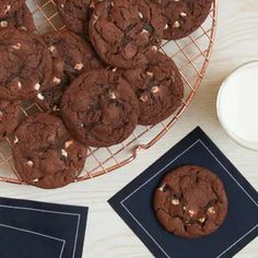 chocolate cookies on a wire rack next to a glass of milk and two coasters