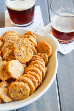 a white bowl filled with crackers next to two glasses of beer