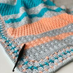 a crocheted blanket with an orange and blue design on it next to a black pen