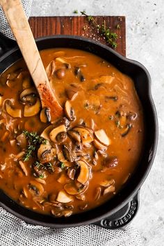 a skillet filled with mushroom soup on top of a wooden cutting board next to a spoon