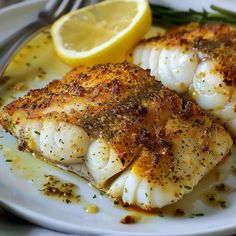 two fish on a white plate with lemon wedges and seasoning next to it