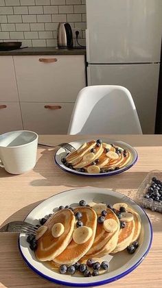 pancakes with blueberries and syrup are served on two plates in front of the kitchen counter