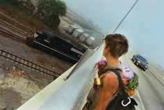 a woman with a backpack is looking out over the tracks at a train and cars