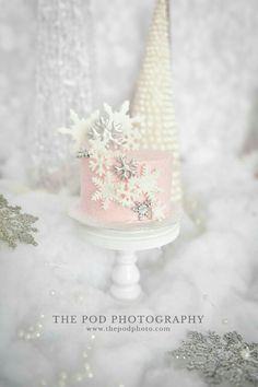 a pink and white cake sitting on top of a table next to snow flakes