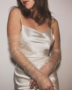 a woman in a white dress with her hands wrapped around her waist and wearing gloves