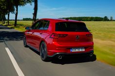 the rear end of a red volkswagen car driving down a road with trees in the background