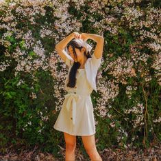 a woman standing in front of a bush with her hands on her head and arms behind her head