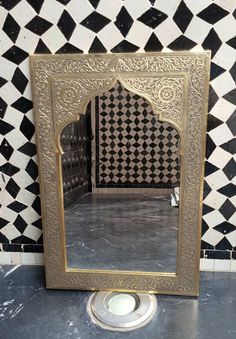 a mirror sitting on top of a tiled floor next to a light bulb in front of a black and white tile wall