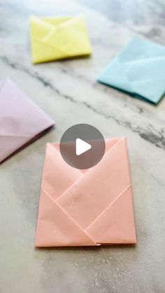 an origami envelope is sitting on a marble table with four different colored envelopes