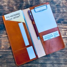 a notebook with a pen and notepad in it sitting on a wooden table next to a clipboard