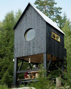 a wooden structure with a round window in the middle of trees and people sitting at a table