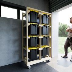 a man standing in front of a shelf filled with black and yellow bins on wheels