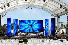 an outdoor stage set up with white chairs and large screens on the wall behind it