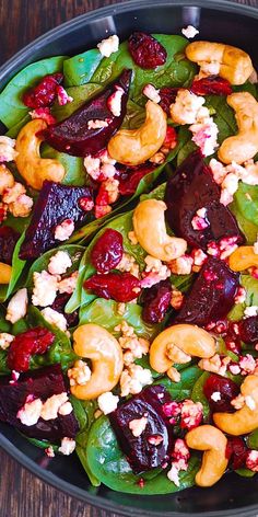 a salad with beets, carrots and nuts in a black bowl on a wooden table