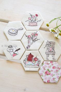 four hexagons with embroidered designs on them sitting on a wooden table next to flowers