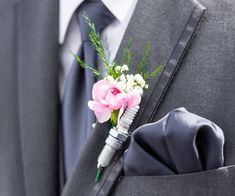 a boutonniere with pink flowers and greenery on the lapel of a suit