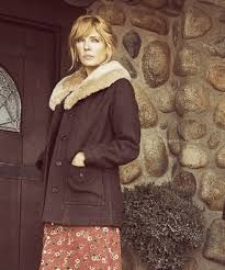 a woman is standing in front of a door wearing a coat and floral print pants