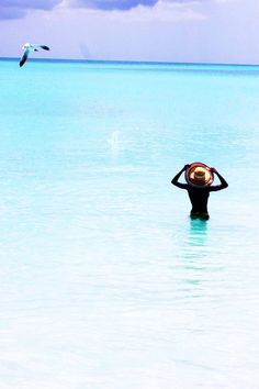 a person standing in the water with a hat on their head and seagulls flying overhead