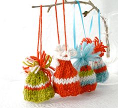 three crocheted bags hanging from a branch on a white tablecloth with blue, green and red ribbons