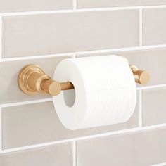 a roll of toilet paper hanging on the wall next to a white brick wall with gold accents