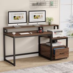 two computer monitors sitting on top of a wooden desk next to a printer and file cabinet