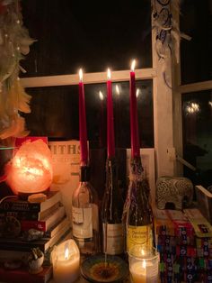 candles are lit in front of bottles and books on a table next to a window