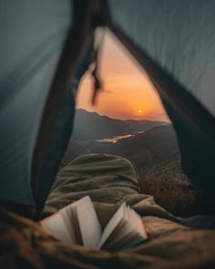 an open tent with a book in it and the sun setting over mountains behind it