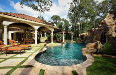 an outdoor swimming pool with lounge chairs around it and a waterfall in the middle, surrounded by greenery