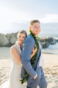 a bride and groom are standing on the beach with their arms around each other as they pose for a photo