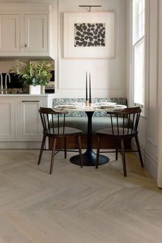 a dining room table and chairs in front of an open kitchen area with white cabinets