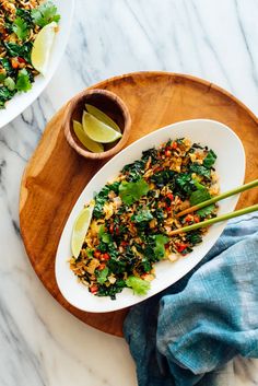 two plates filled with food on top of a wooden tray next to a bowl of lime wedges