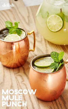 two moscow mules with lime and mint garnish in copper mugs on wooden table