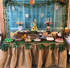 a table topped with lots of cakes and desserts next to a window covered in greenery